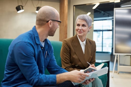 Two middle-aged male and female colleagues discussing and taking notes 